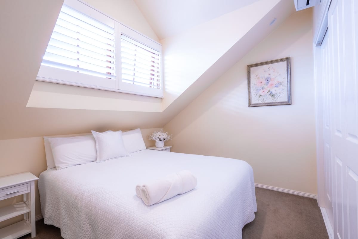 Cottage queen bedroom with white linens and pitched ceiling